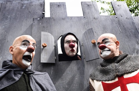 Tre clowner i riddarkläder vid ett grått slott.